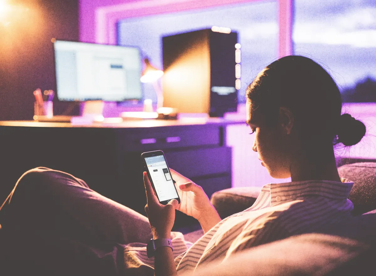 Koltuğunda oturan bir kullanıcı, telefonundan odanın diğer ucundaki bilgisayarına bağlanıyor